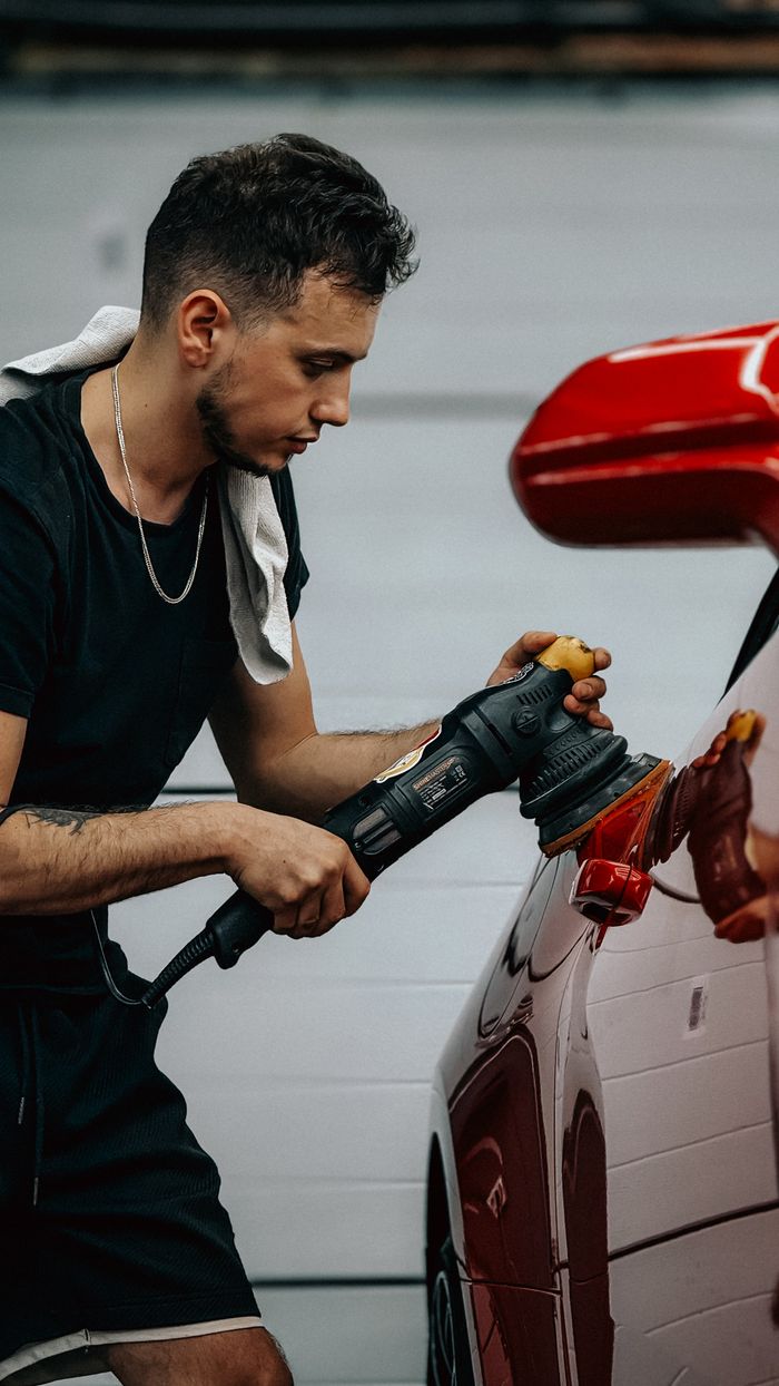 Mastering the First Impression: Your intriguing post title goes here A focused man polishing a shiny red car with an electric buffer in a modern garage.