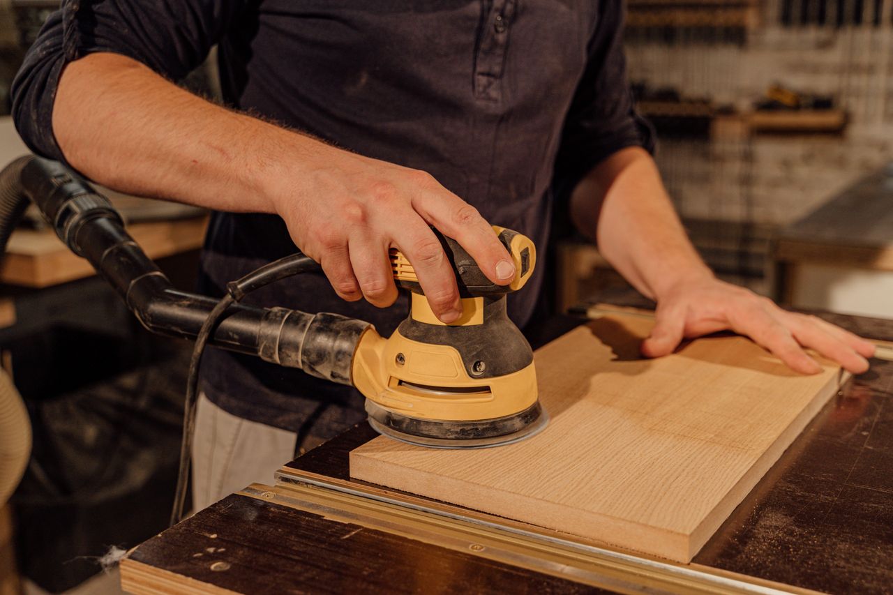 The Art of Drawing Readers In: Your attractive post title goes here Carpenter using an electric sander on a wooden board in a workshop, showcasing craftsmanship.