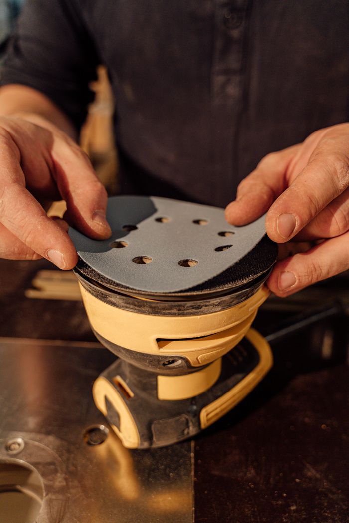 Crafting Captivating Headlines: Your awesome post title goes here Hands carefully attaching a sanding pad to an industrial machine in a workshop setting.