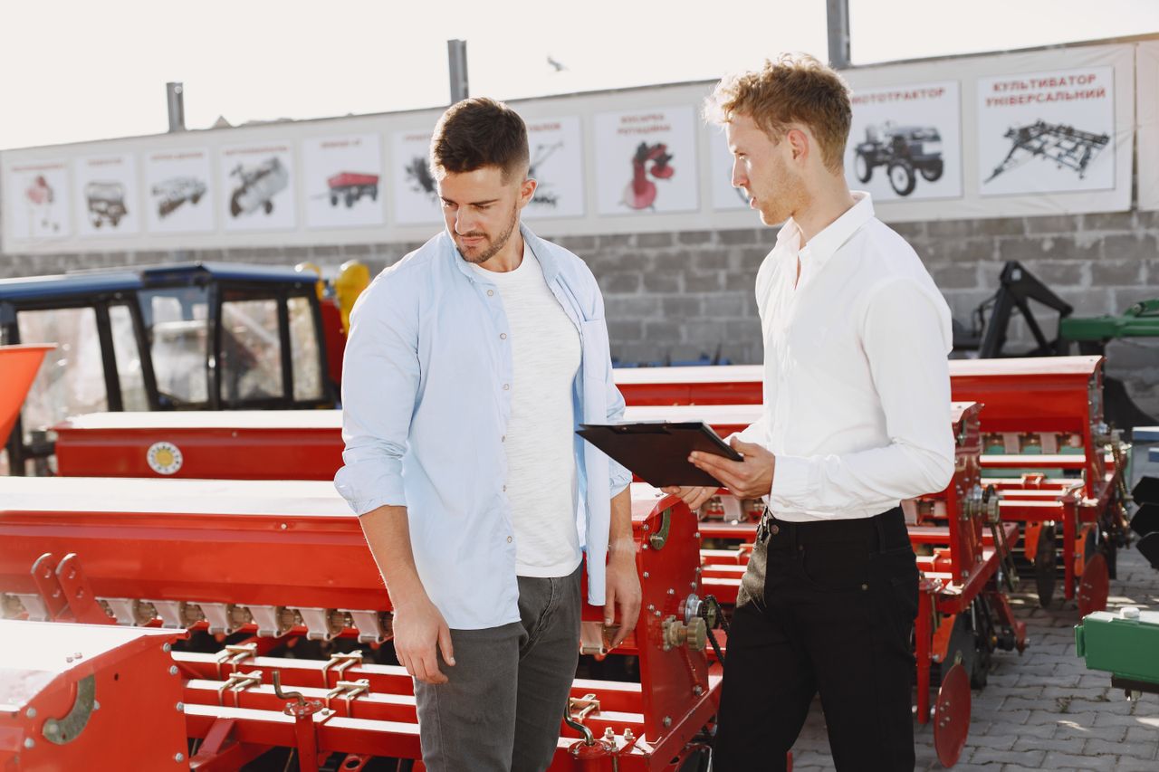 Services Two men discussing agricultural equipment at an outdoor store during the day.